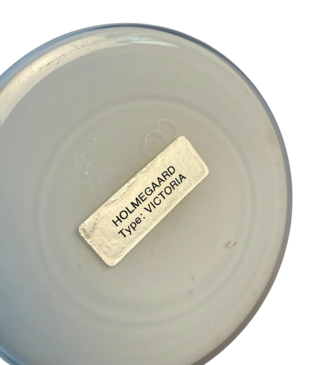 Modighus.se etikett på undersidan av en vit Holmegaard Viktoria fotogenlampa i glas från 1960-talet