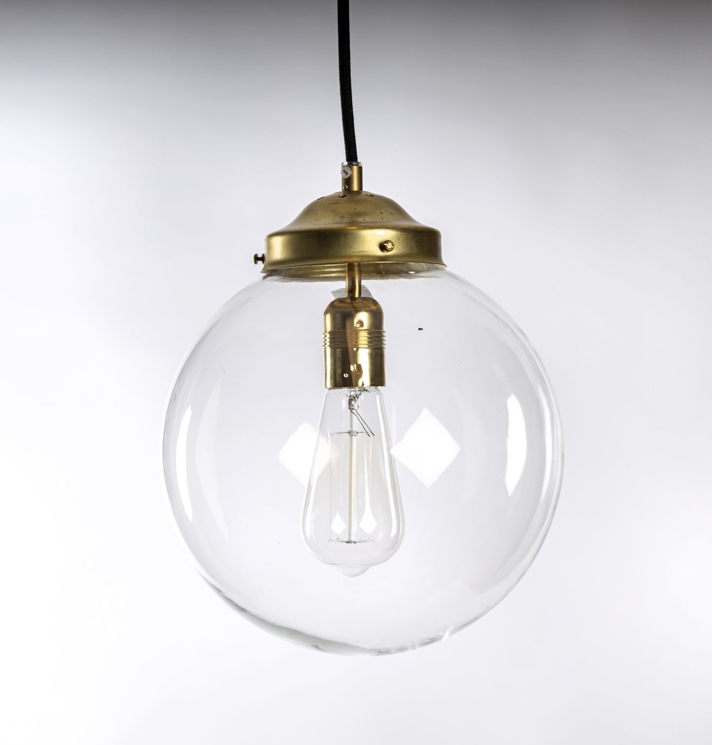 Taklampa med klarglas glob, mässingsfäste och svart rund textilkabel, passar koltrådslampa, 1950-tal
