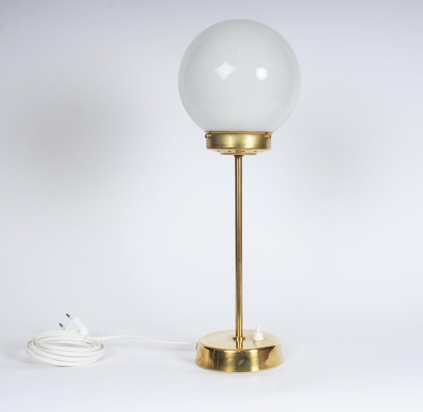 Elegant bordslampa med stomme i mässing och stor vit glasglob. 
