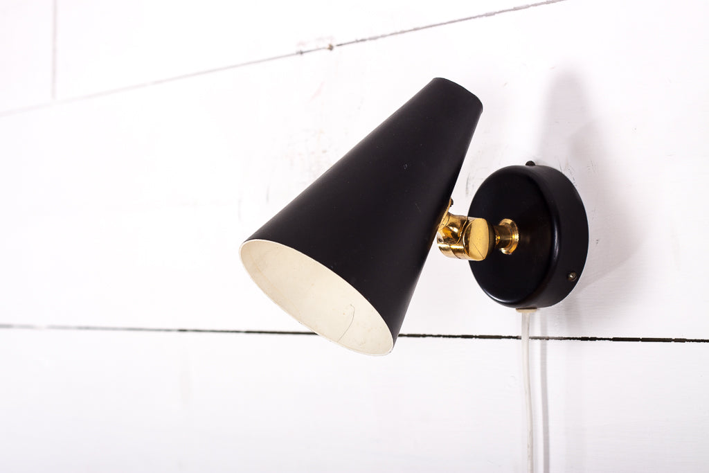 Stilren retro vägglampa i svart metall med detaljer i mässing. 

