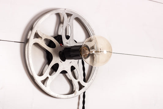 Unik vägglampa formad som en gammal filmrulle med svart tvinnad tygkabel.
