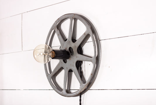 Unik vägglampa formad som en gammal filmrulle med svart tvinnad tygkabel. 
